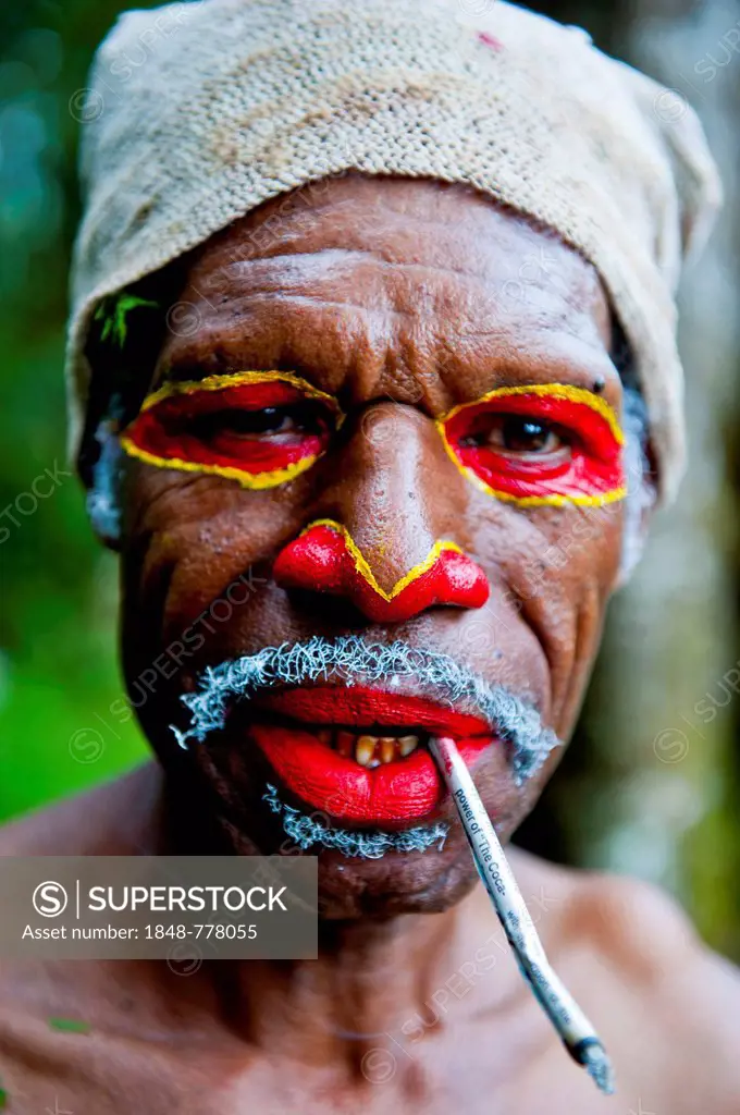 Man with colourful face paint smoking a cigarette is celebrating at the traditional Sing Sing gathering in the highlands