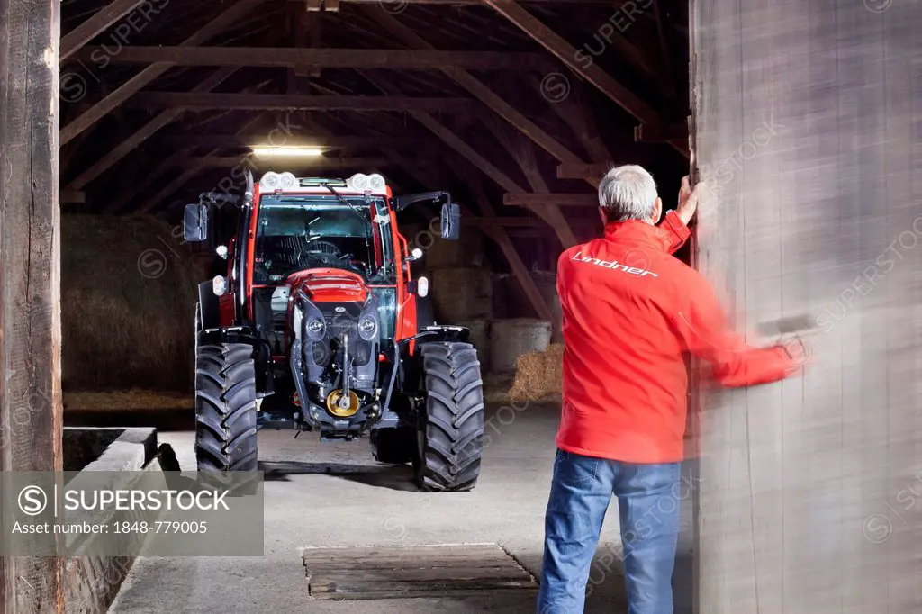Farmer opening a barn door revealing a tractor behind it