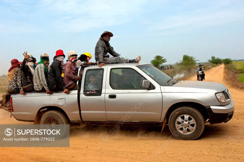 Small pickup truck carrying farm workers in the crowded cargo bay on a country road