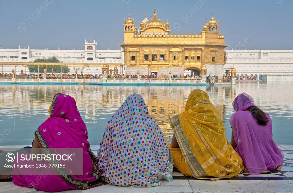 Indian women, pilgrims wearing colorful saris sitting on the edge of the water basin of the Amrit Sagar, or Holy Lake, Harmandir Sahib or Hari Mandir ...