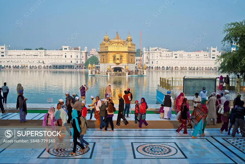 Sikh pilgrims walking around the Amrit Sagar or Holy Lake, Harmandir Sahib or Hari Mandir or Golden Temple, the most important Sikh temple, at the bac...