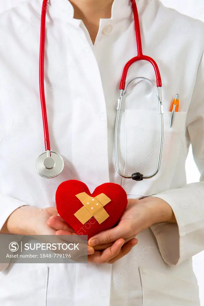 Female doctor holding a red heart with a plaster in her hands, symbolic image for a heart attack