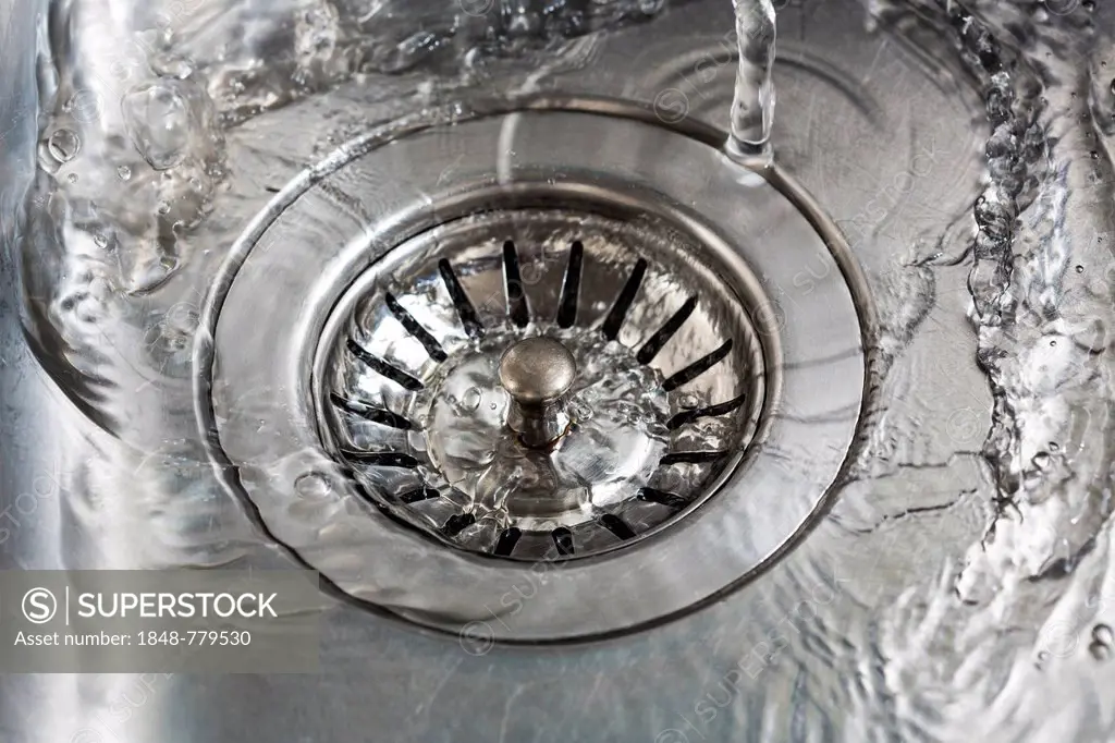 Water flowing into the drain of a sink, symbolic image for water consumption, water wastage