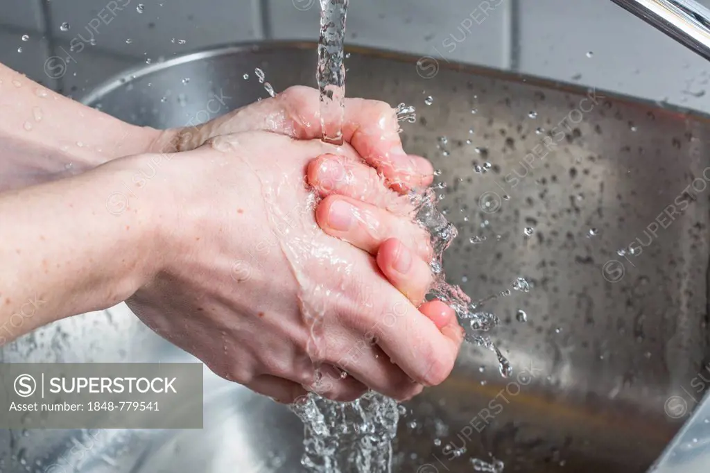 Person washing their hands under running water from a faucet, symbolic image for water consumption