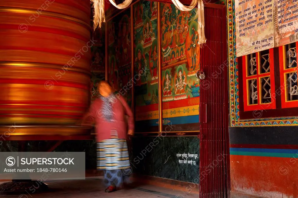 A female devotee spinning a large prayer wheel