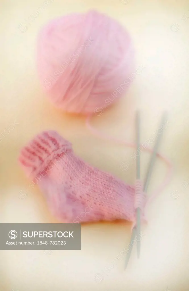 Semi-finished knitted pink baby sock with a ball of wool and knitting needles