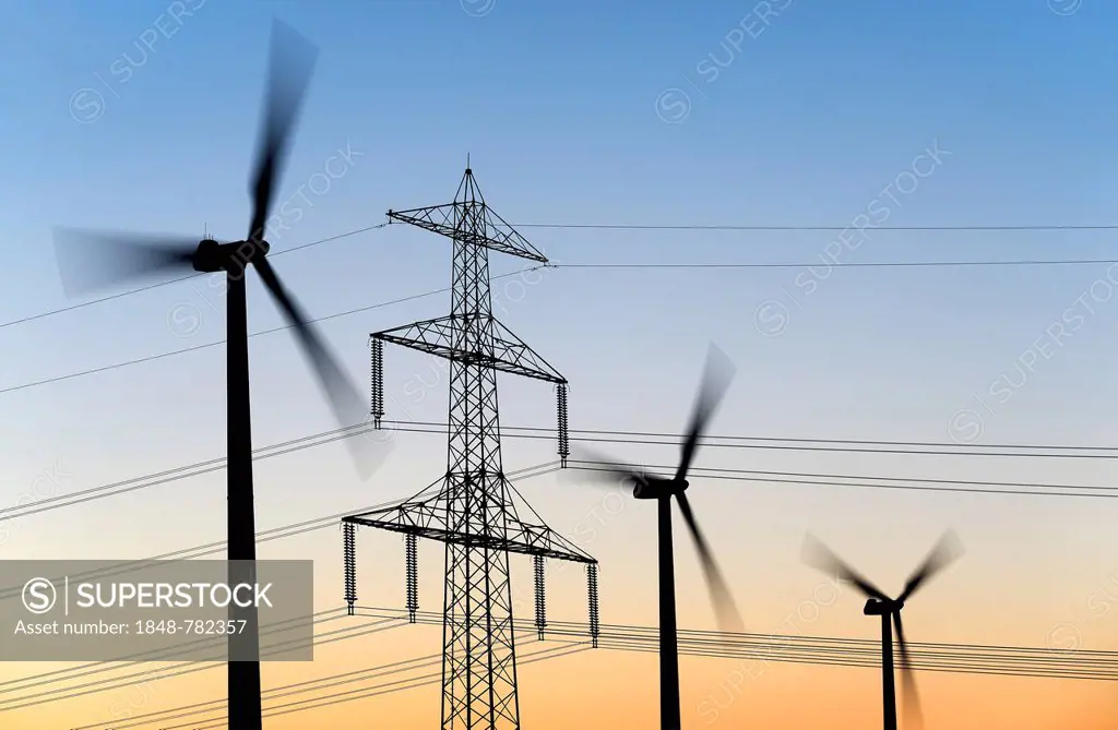 High voltage transmission tower and wind turbines at dusk