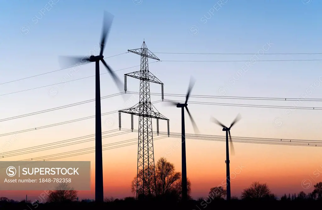 High voltage transmission tower and wind turbines at dusk