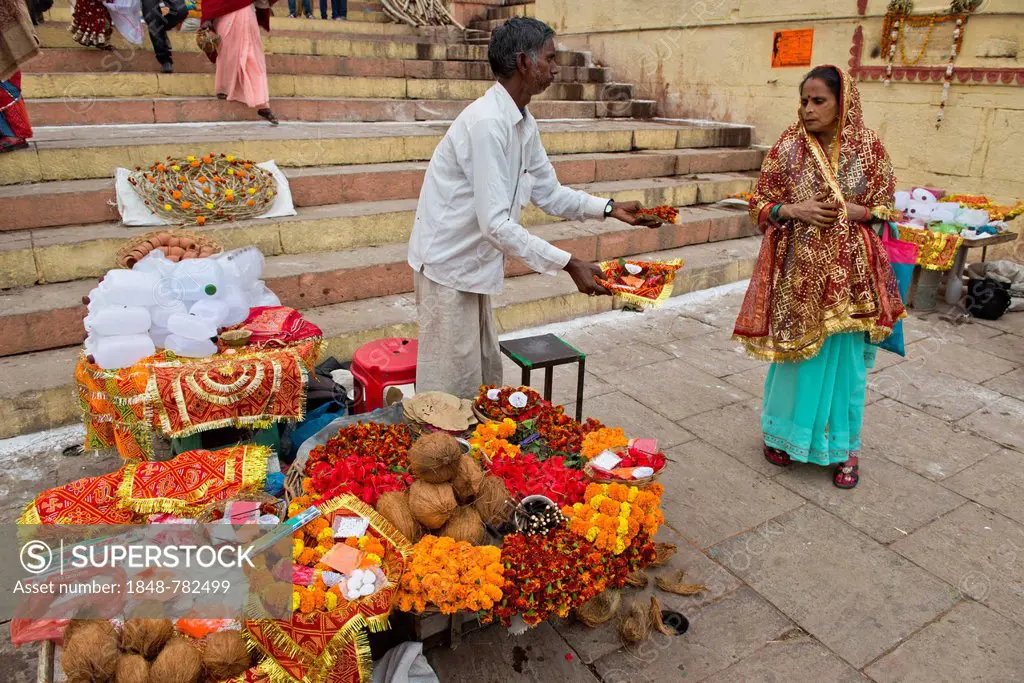 Man at a stall offering small bowls with flowers and ritual offerings to a passing woman, the sacrificial bowls are offered in honour of the Mother Go...