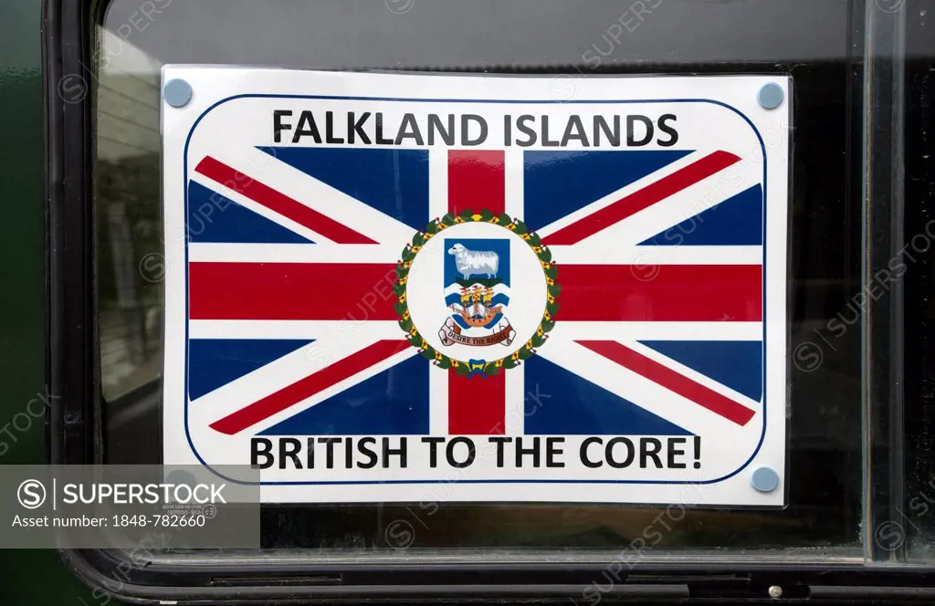 Sign Falkland Islands - British to the Core with a coat of arms and the flag of the Falkland Islands, displayed in a car window as a protest against A...