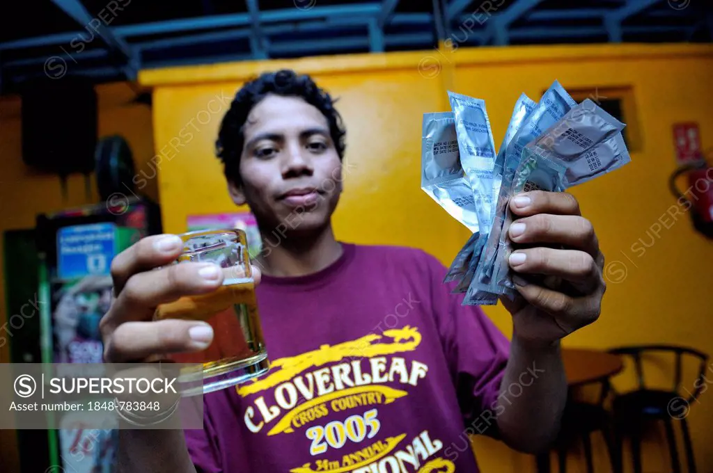 Young man in a brothel holding a beer and condoms in his hand, protection against AIDS and other sexually transmitted diseases *** No publication in N...