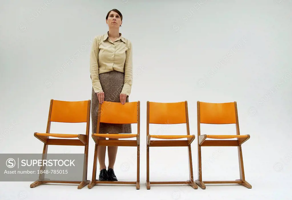 Woman wearing conservative clothes standing behind a row of orange chairs
