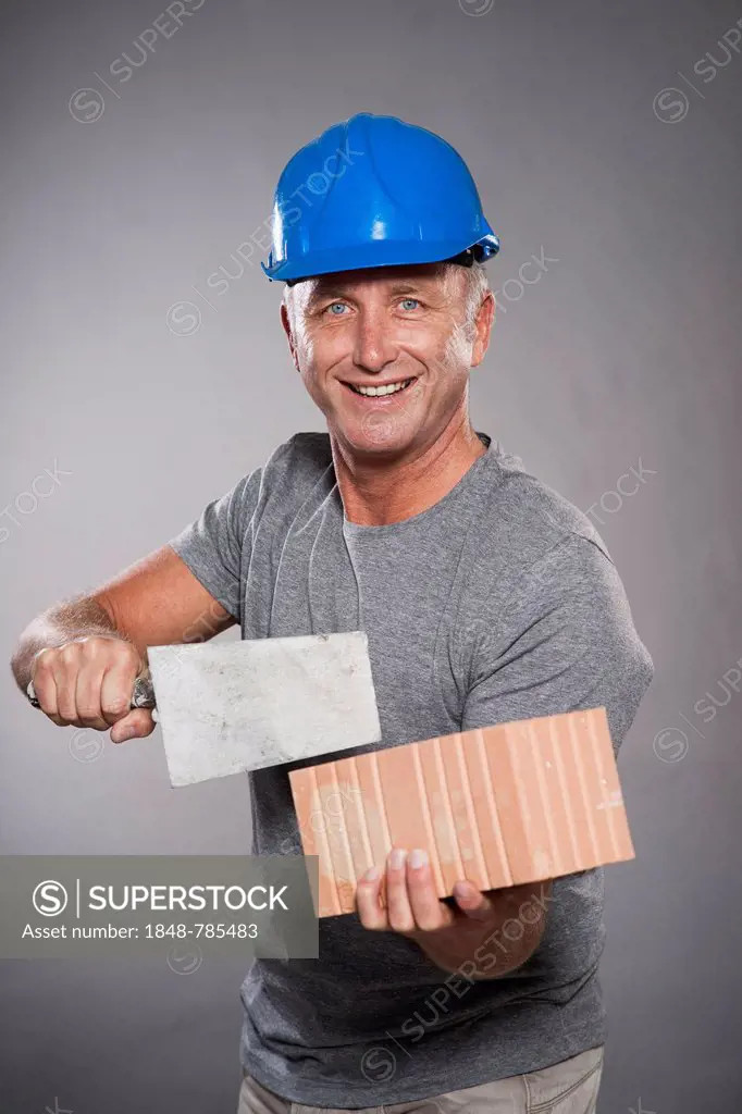 Construction worker wearing a hard hat, holding a trowel and a brick
