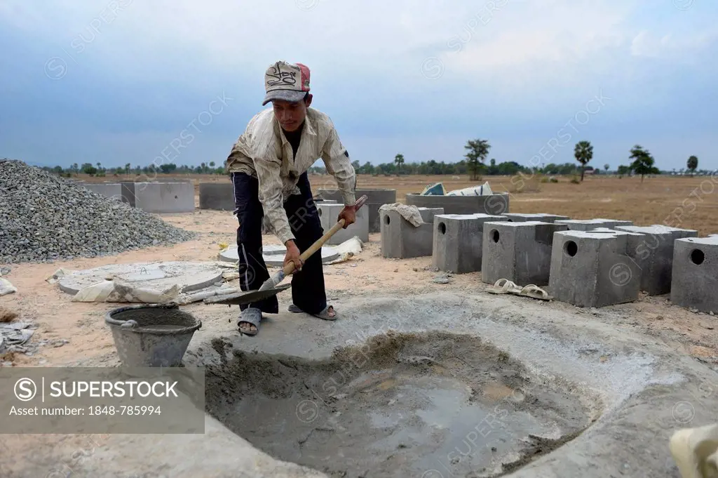 Young man in a local construction company mixing cement to produce parts for latrines, rear