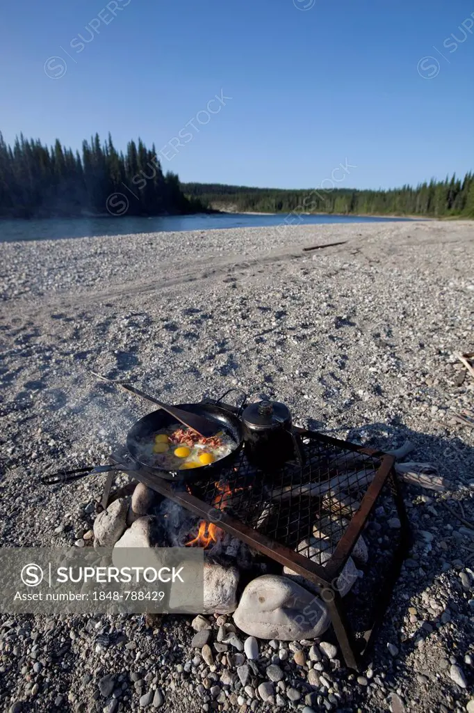cooking / frying bacon and eggs on a camp fire, pot, pan, spatula, gravel bar, upper Liard River, Yukon Territory