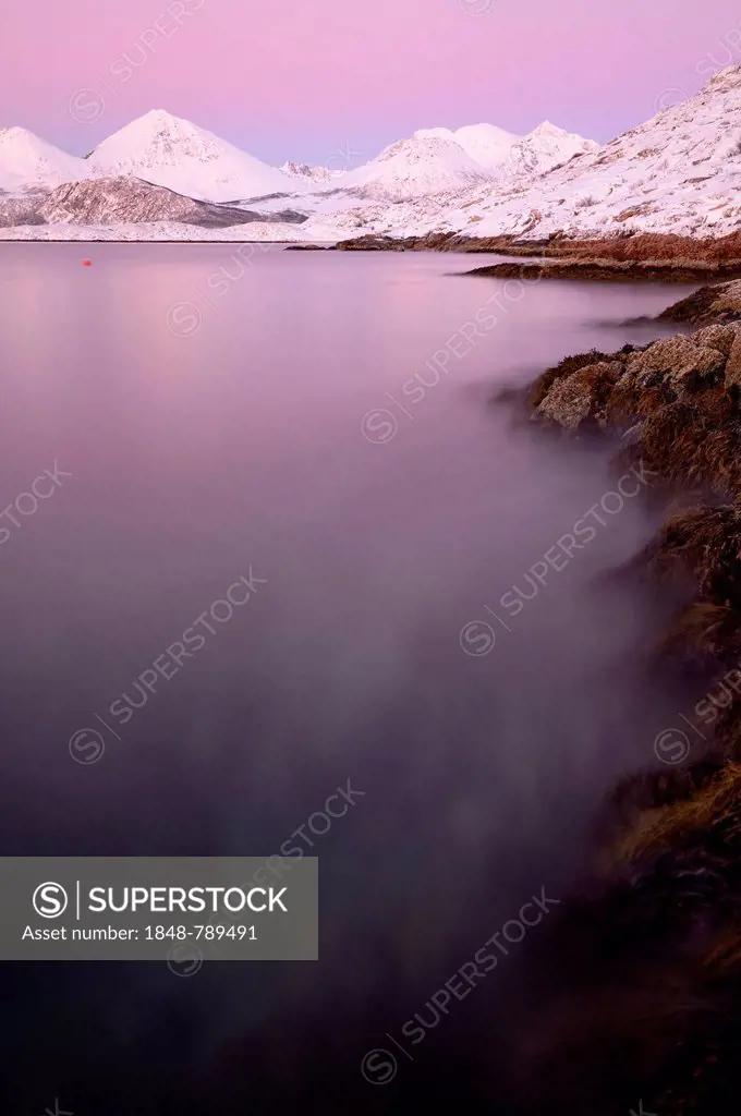 Fjord with stones in front of a mountain range in the evening light