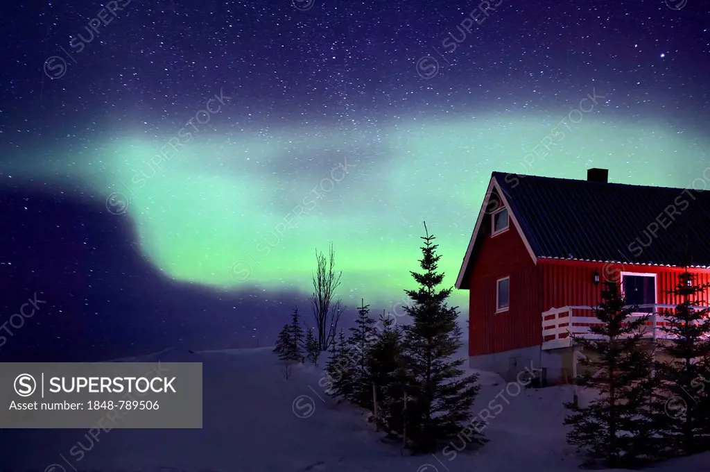 Red Norwegian house with an aurora in winter