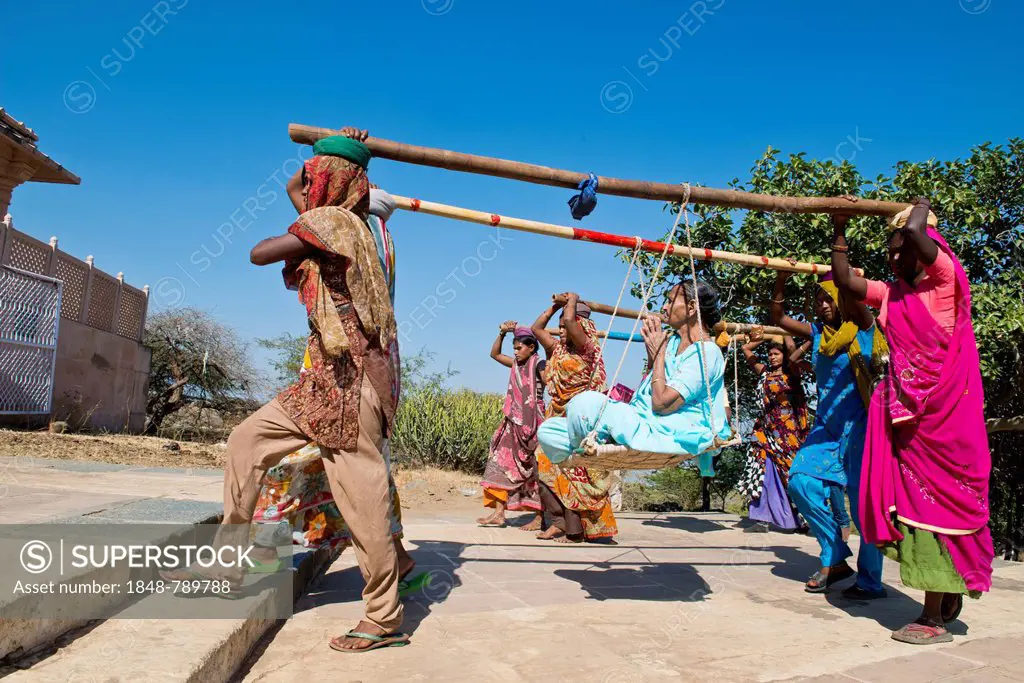 Young Indian women wearing traditional saris carrying long bamboo poles on their heads with a seat for pilgrims climbing the steps to the temple compl...