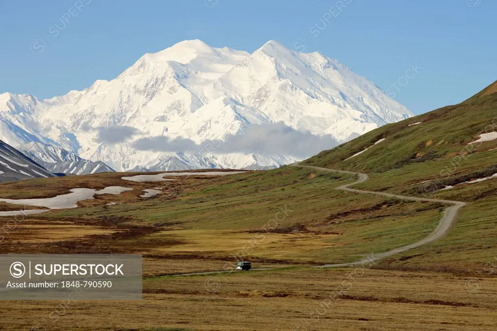 A shuttle bus from the Denali National Park and Preserve crossing the tundra with views of Mt McKinley at back