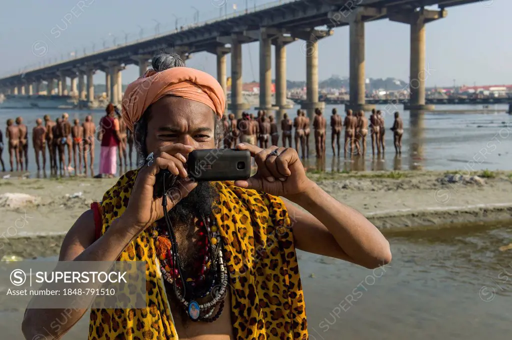 Shiva sadhu, holy man, taking a photograph with his mobile phone at the Sangam, the confluence of the rivers Ganges, Yamuna and Saraswati, during Kumb...