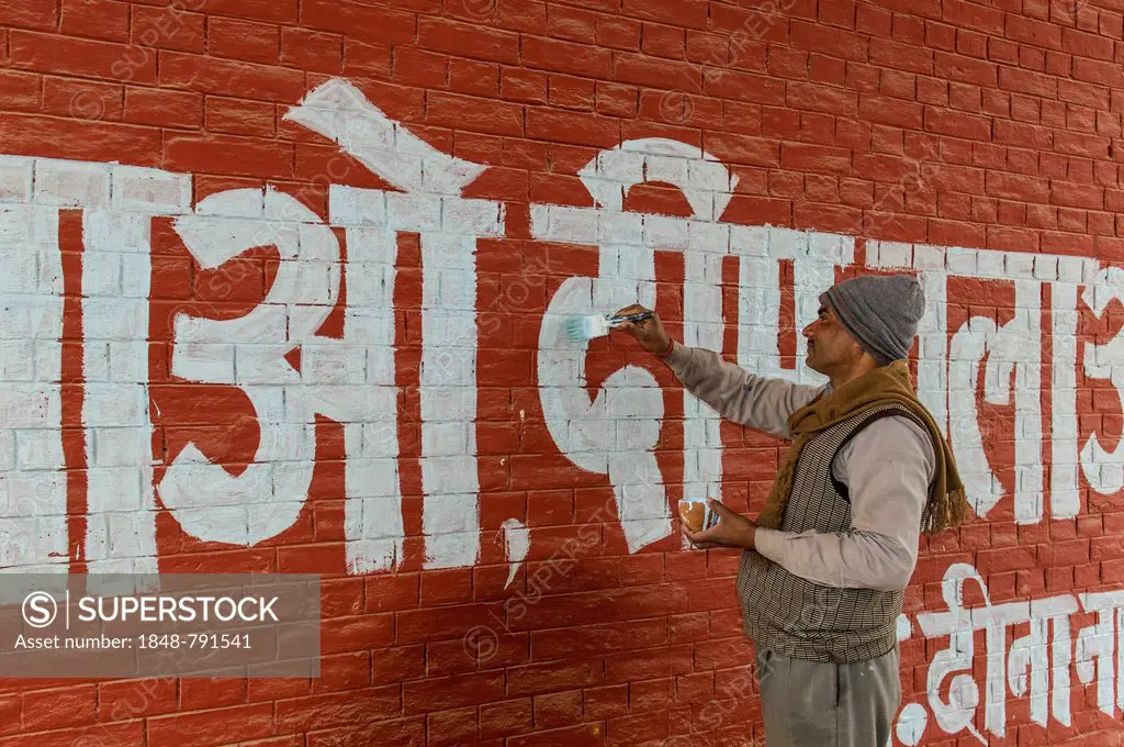 Man painting white letters in Hindi language onto a red wall
