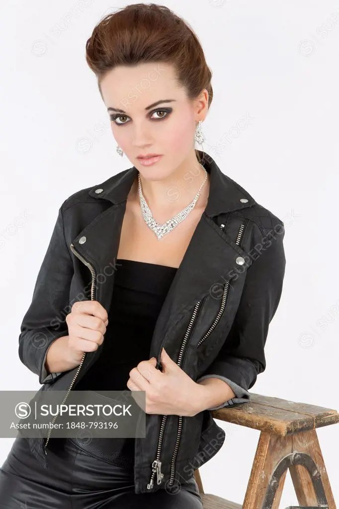 Young woman in a black leather outfit posing with an old wooden ladder