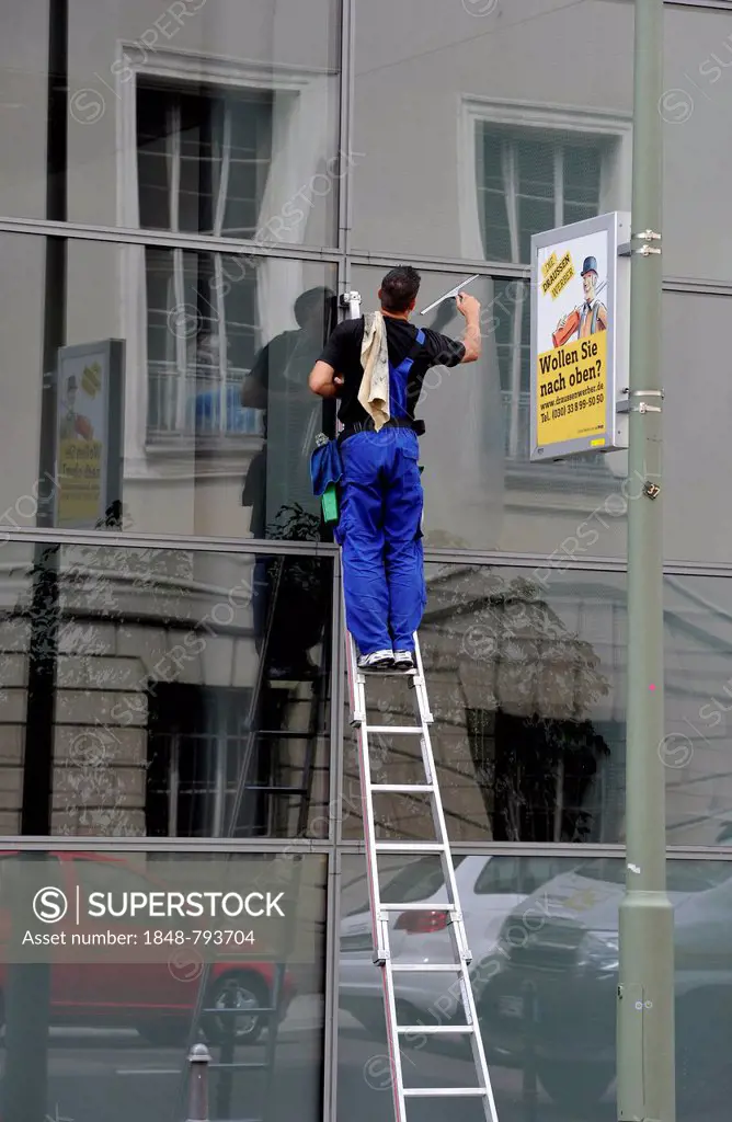 Window cleaner standing on a ladder cleaning a glass façade, next to advertising sign Wollen Sie nach oben, German for do you want to climb the socia...