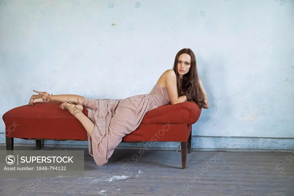Young woman lying on a chaise longue in a room in need of redecoration