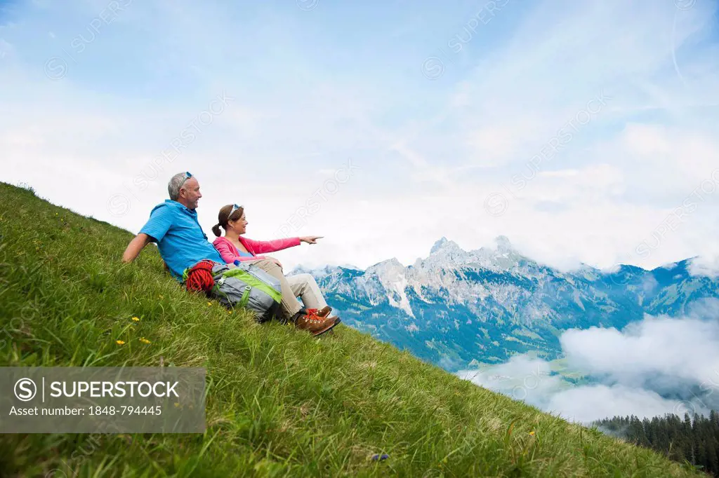 Hikers sitting on a mountain meadow and enjoying the view of the Tannheim mountains