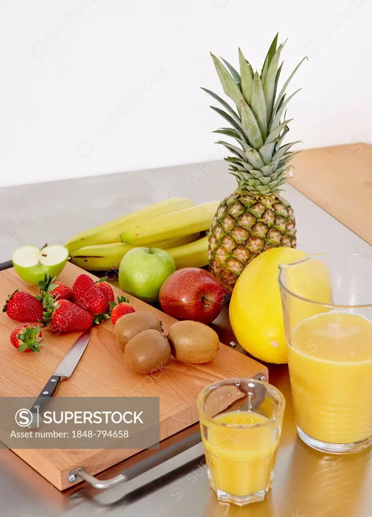 Various types of fruit on a cutting board, orange juice to one side