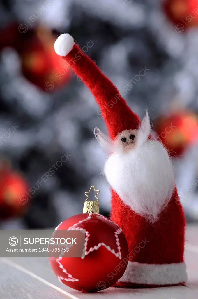 Red Christmas bauble and a felt Santa Claus in front of a Christmas tree