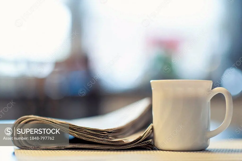 A cup of coffee and a newspaper lying on a kitchen table, Germany, Europe