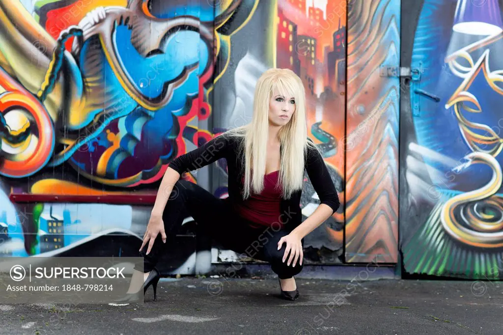 Young woman with long blonde hair posing in front of a wall with graffiti