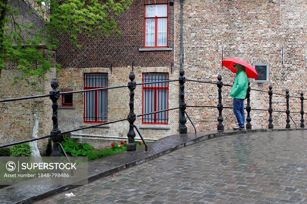 Woman with red umbrella in rain on bridge at Begijnhof nunnery