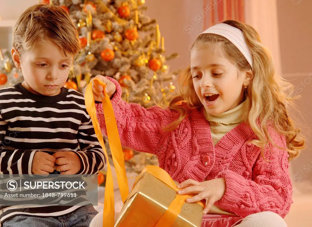 Girl and boy unpacking a gift in front of a Christmas tree