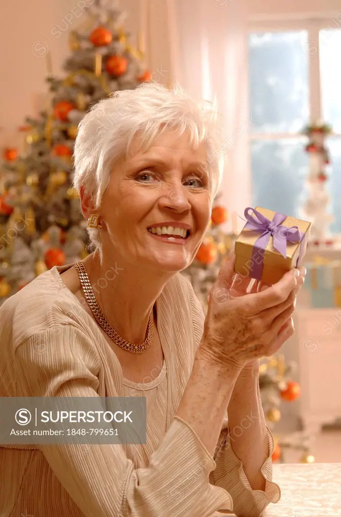 Mature woman holding a gift in front of a Christmas tree