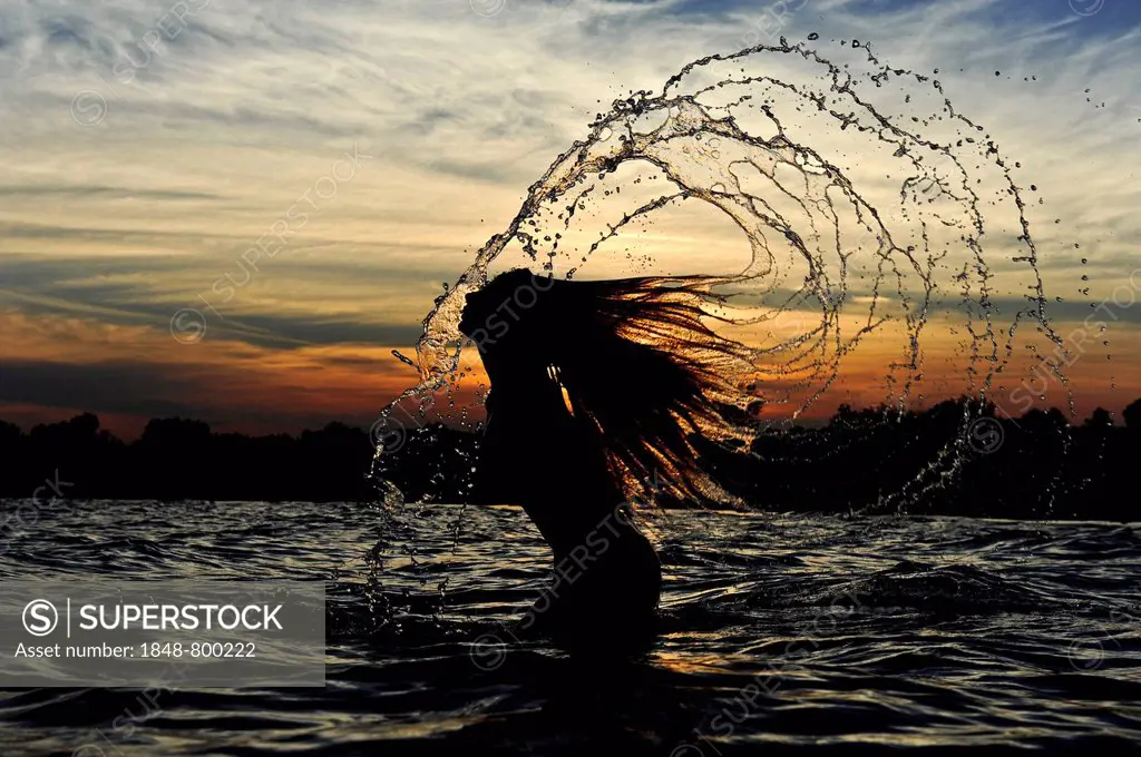 Young woman standing in the sea throwing back her long hair with splashing water, sunset on the Adriatic Sea, Jesolo, Italy, Europe