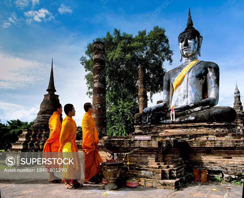Three monks standing in front of the seated Buddha at Wat Mahathat, temple ruins, pillars, chedi, Sukhothai Historical Park, Sukhothai, Sukhothai Prov...