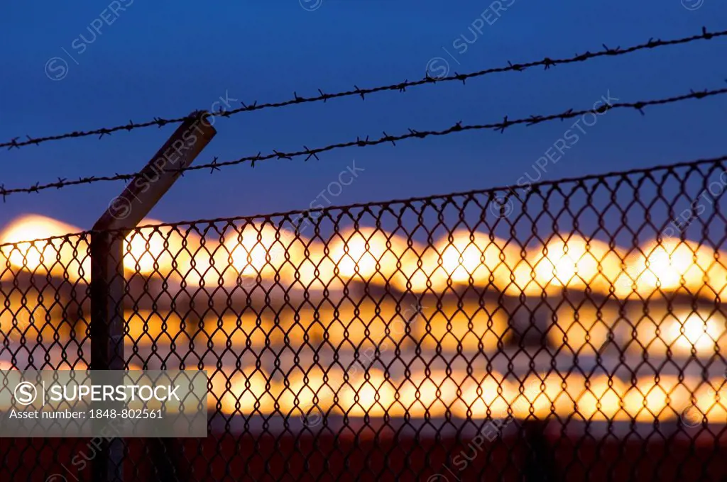 Roped off. Fence with barbwire in front of a factory hall in the evening.