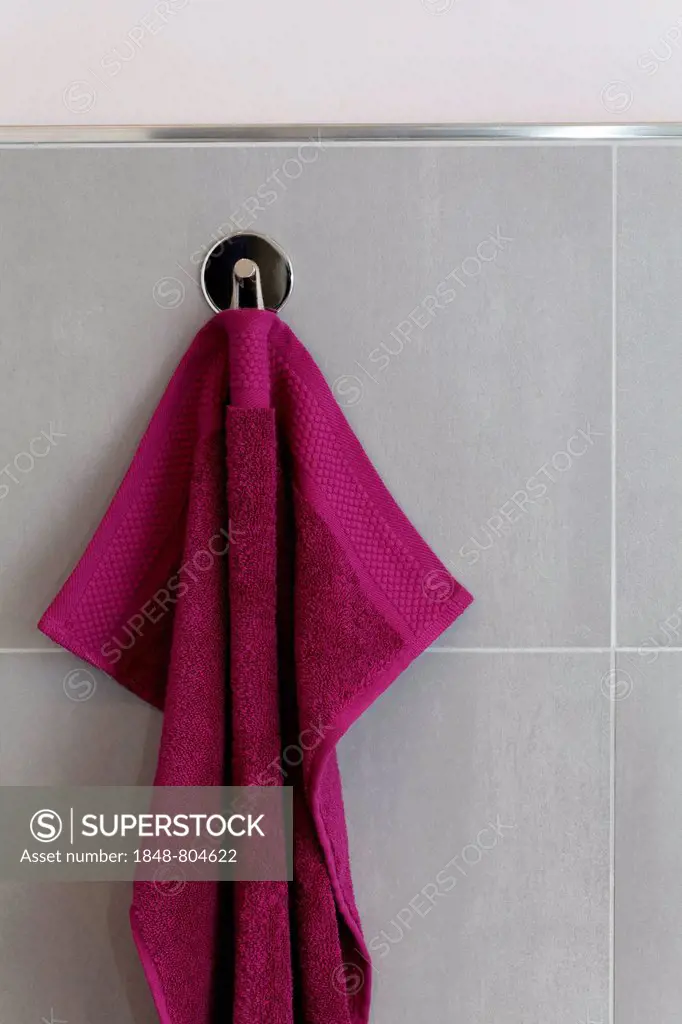 Berry-colored towel hanging on a hook, tiled wall, bathroom