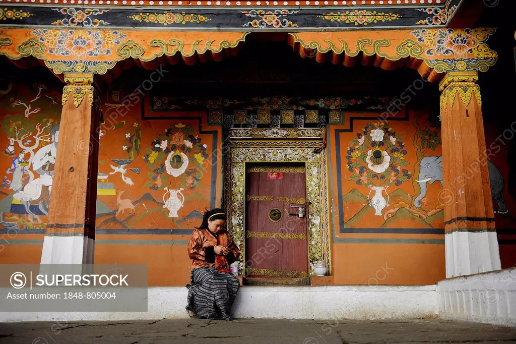 Young woman sitting in front of the ornate entrance of a side temple at the Paro Dzong, Rinpung Dzong fortress, Paro, Paro district, Bhutan