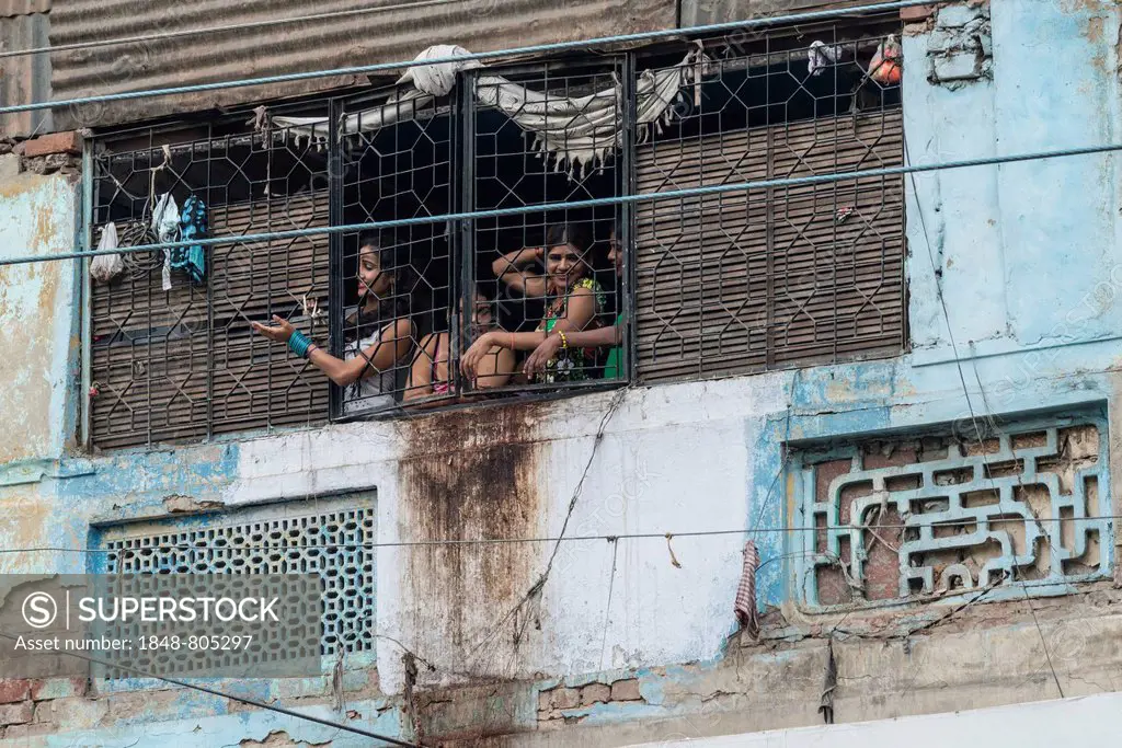 Prostitutes looking out of a window secured with bars waving to potential customers in the redlight district, New Delhi, Delhi, India