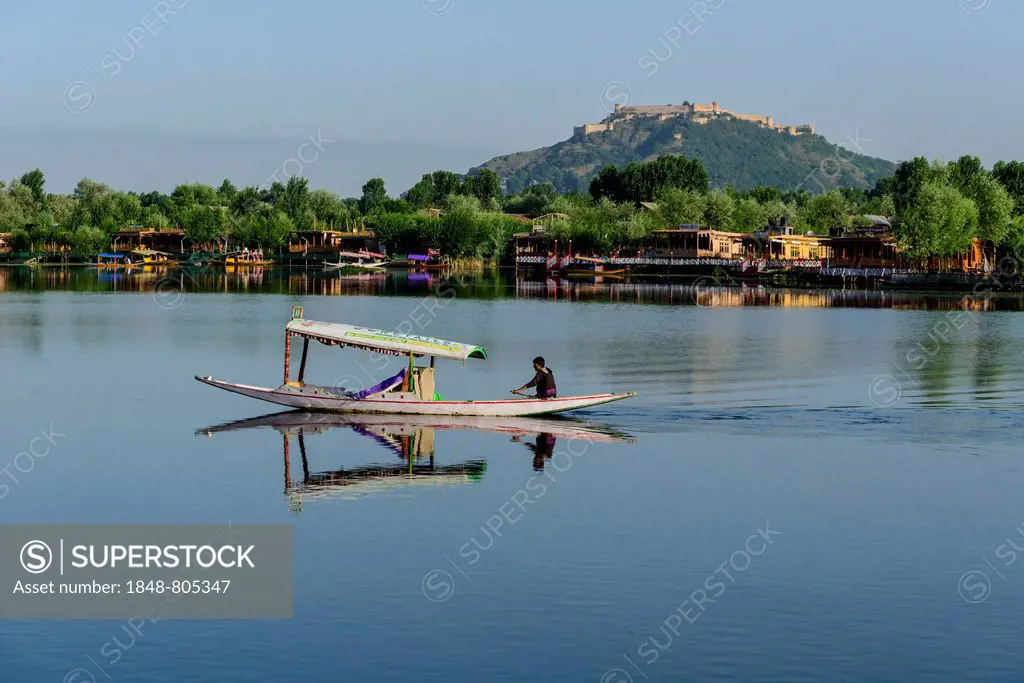 A shikara boat crossing Dal Lake, houseboats and the Durrani Fort on Hari Parbat hill at the back, Srinagar, Jammu and Kashmir, India
