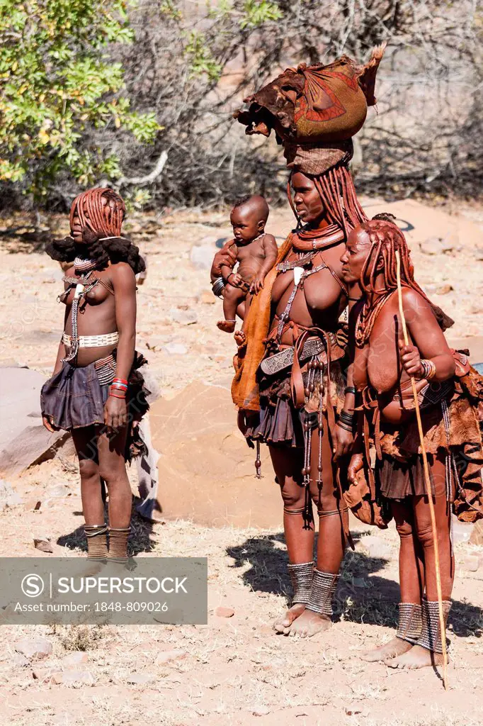 Three traditionally dressed Himba women, one holding a baby, bei Ruacana, Omusati Region, Namibia