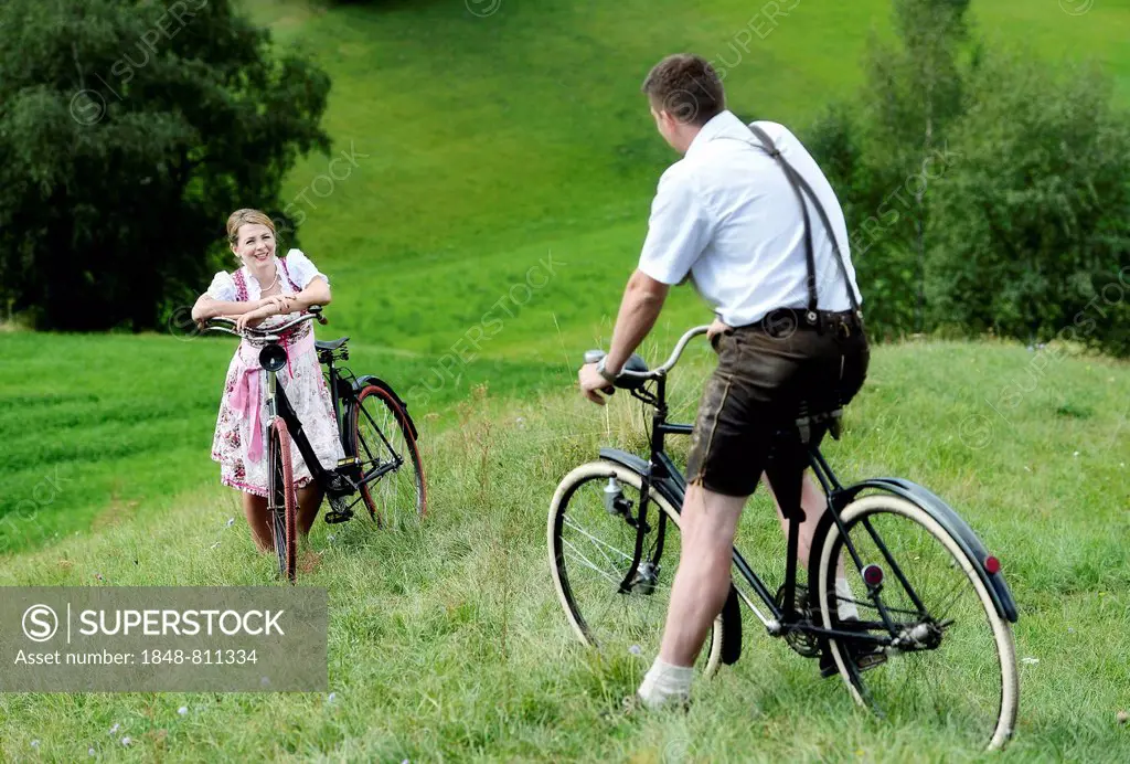 Man wearing leather pants and a woman wearing a dirndl on old bicycles within a natural landscape, Igls, Innsbruck, Tyrol, Austria