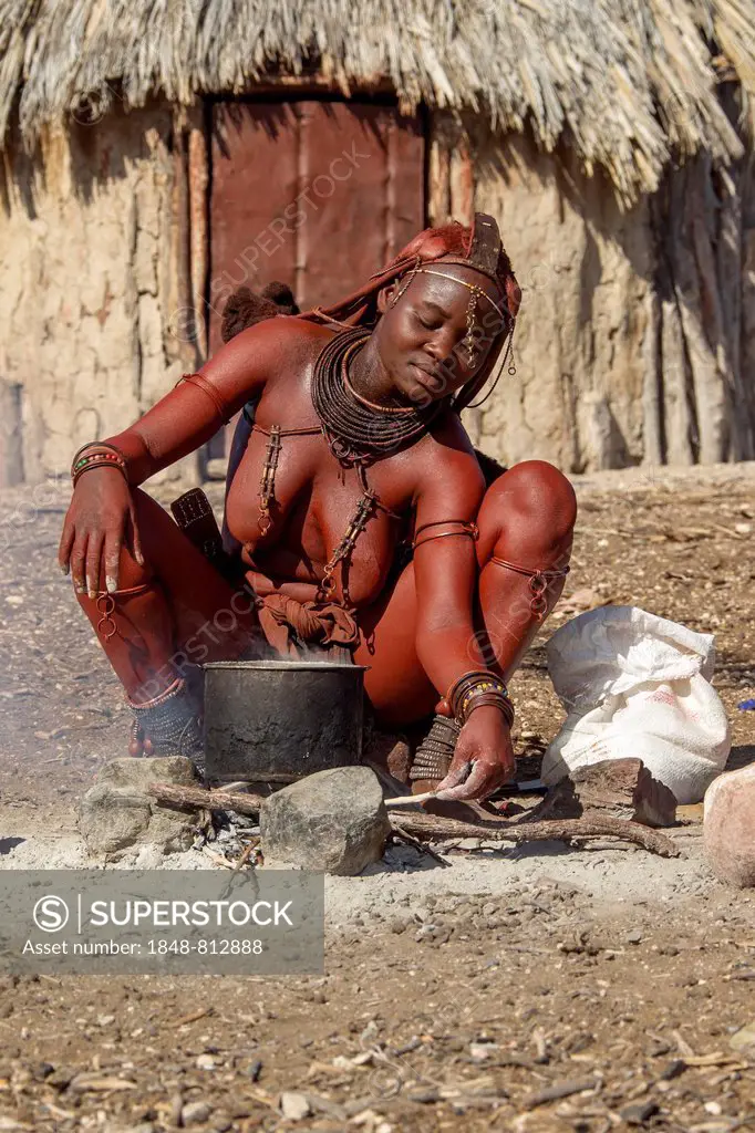 Young Himba woman, sitting at a cooking pit in front of a hut, Kaokoland, Kunene, Namibia
