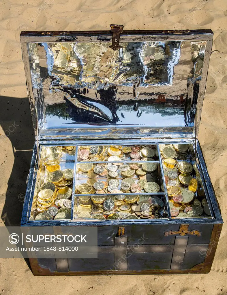 Treasure chest with gold and silver coins on the sand