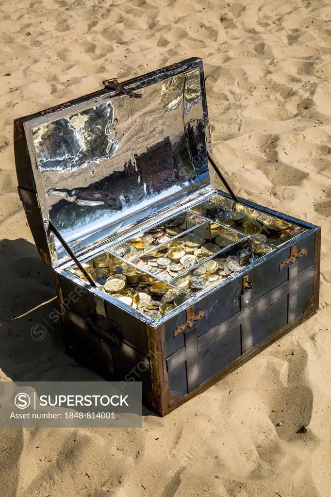 Treasure chest with gold and silver coins on the sand