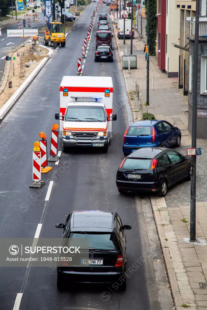 Ambulance driving against the traffic at a construction site during an emergency operation, other cars driving off the road to allow free passage, Ess...