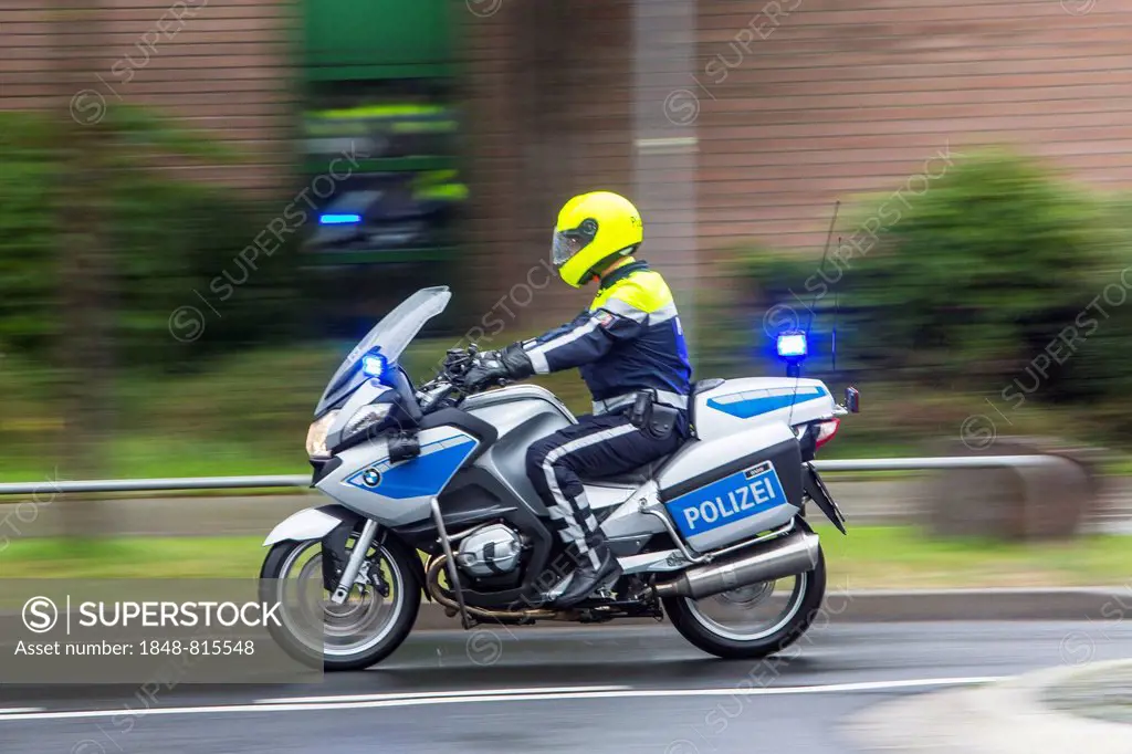 Policeman wearing yellow a helmet on a motorcycle, police motorcycle patrol of the NRW Police riding with flashing blue lights during an emergency ope...